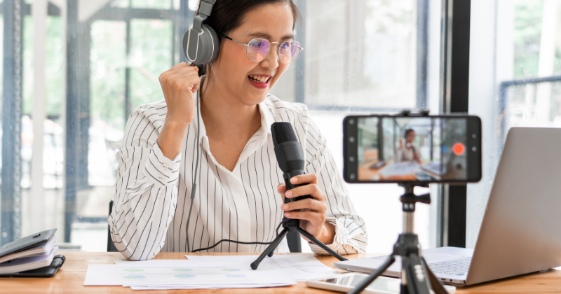 An Asian woman is using AI podcast tools to record a video with a microphone in front of a laptop.